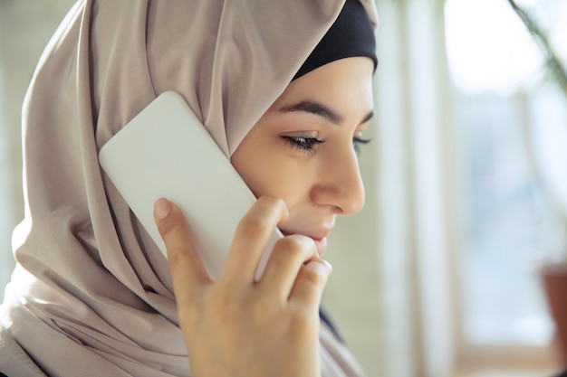 Falando ao telefone, sorrindo. Feche o retrato de uma bela mulher de negócios árabe usando hijab enquanto trabalha no openspace ou escritório. Conceito de ocupação, liderança, sucesso, solução moderna.