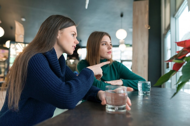 Falando de mulheres jovens, meninas sentado no café, sorrindo e conversando, bebendo água limpa em vidro