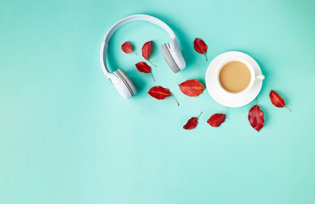 Fallen sie flach legen zusammensetzung mit roten herbstblättern, tasse kaffee und weißen kopfhörern auf blauem hintergrund. herbst-podcast-hintergrund. herbst-playlist-konzept.