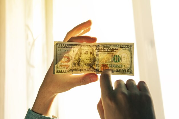 Falschgeld-Licht prüfen. 100 Dollar gegen das Fenster in seiner Hand. Suchen Sie nach Wasserzeichen auf dem neuen Hundert-Dollar-Schein. Transparenz der amerikanischen Währung.