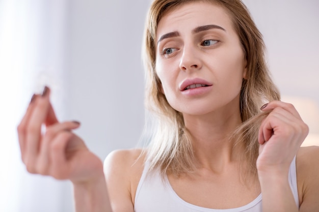 Falta de vitaminas. Mechón de cabello en manos de una triste mujer con bajo peso mientras lo mira