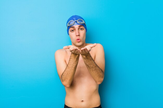 Faltende Lippen des jungen Schwimmermannes und Halten von Palmen senden Luftkuss.
