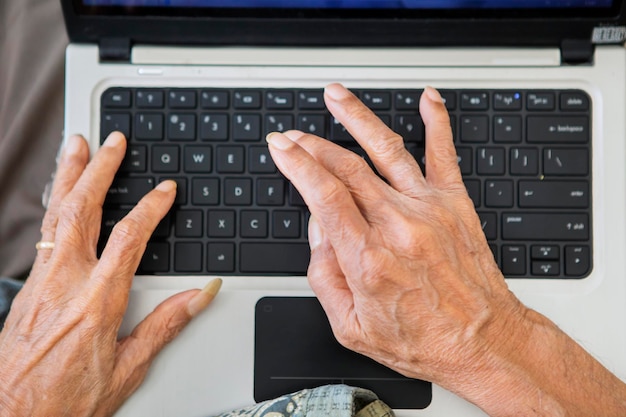 Faltige Hände eines alten Mannes, der auf dem Laptop tippt