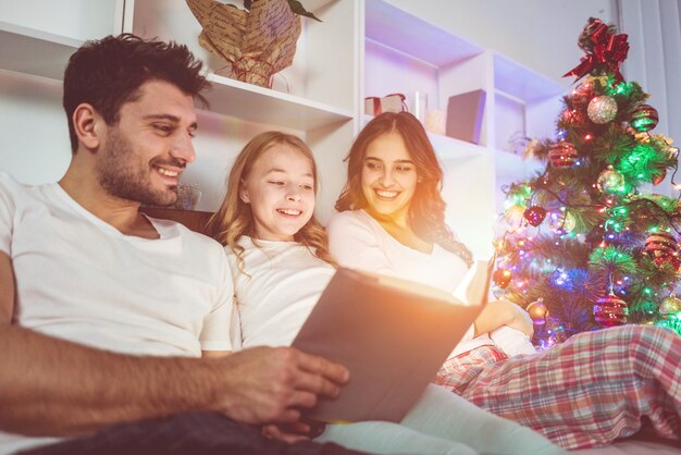 La familia se acostó y leyó el libro cerca del árbol de Navidad. tiempo de la tarde