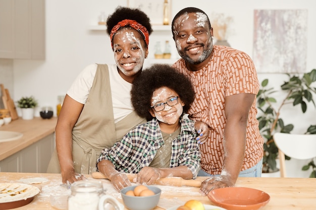 Família africana alegre e divertida de três pessoas em pé na mesa da cozinha