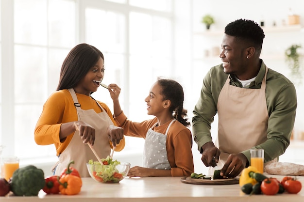 Família africana alimentando uns aos outros se divertindo preparando salada interior