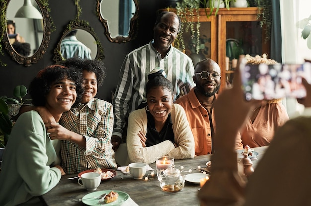 Familia africana feliz sonriendo a la cámara en el teléfono móvil mientras se sienta en la mesa de comedor en casa