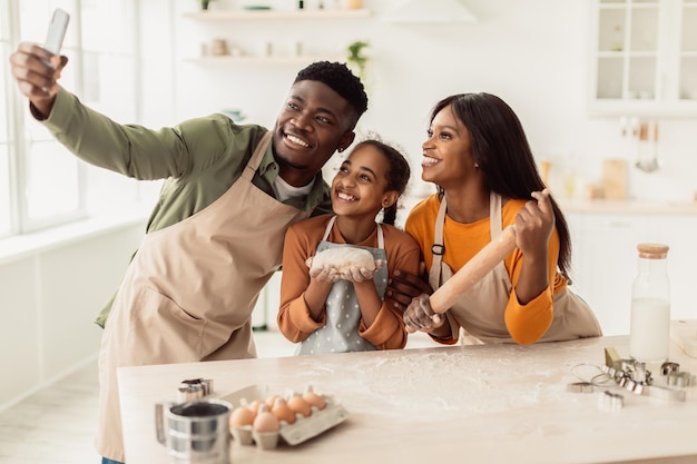 Familia africana horneando galletas haciendo selfie sosteniendo masa en la cocina