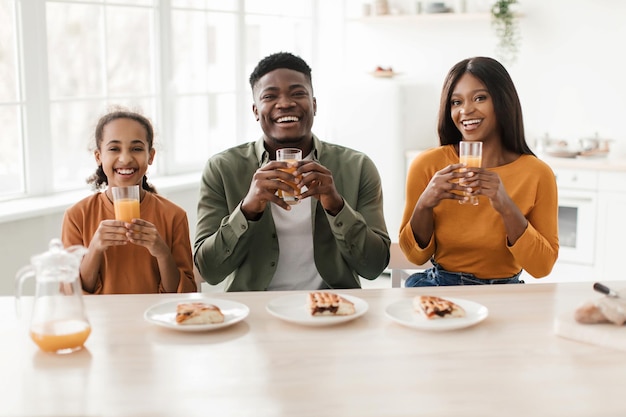 Familia africana sosteniendo vasos bebiendo jugo de naranja fresco en la cocina