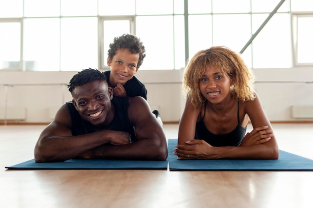 Família afro-americana em roupas esportivas deitada em tapete de ioga e sorrindo