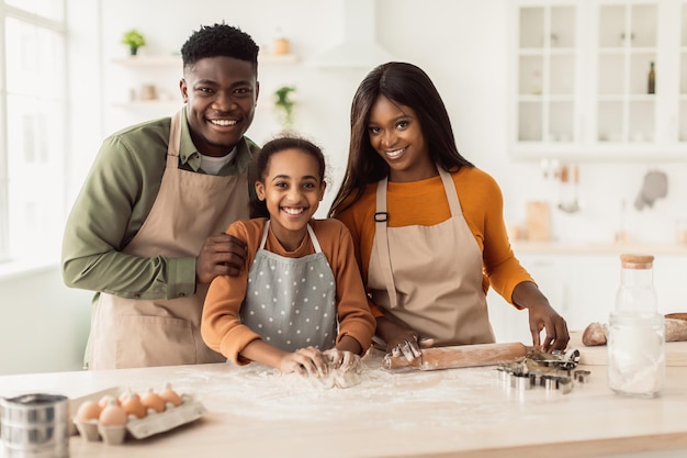 Família afro-americana feliz assando massa de amassar na cozinha