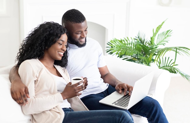 Família afro-americana jovem navegando na internet no laptop em casa, esposa bebendo café