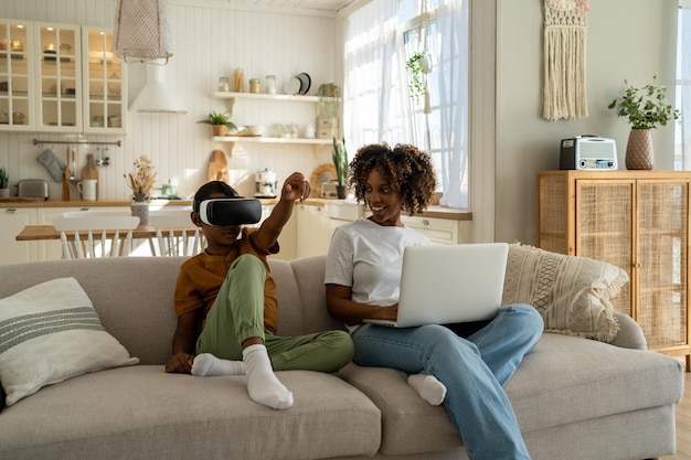 Foto família afro-americana moderna mãe e filho sentam-se no sofá com dispositivos eletrônicos tecnologia e crianças