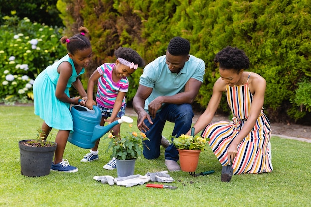 Família afro-americana regando plantas juntas no jardim do quintal