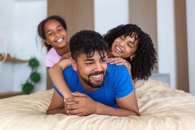 Família afro-americana sorridente de três deitada na cama, uma em topone em midlle e outra em baixo
