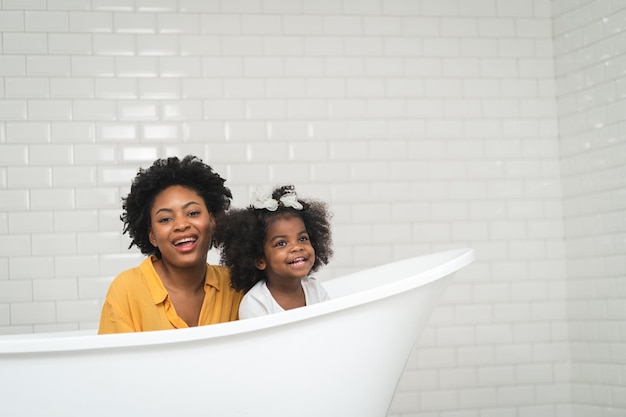Foto familia afroamericana feliz madre e hija divirtiéndose y jugando juntos en el fondo de la pared blanca del baño