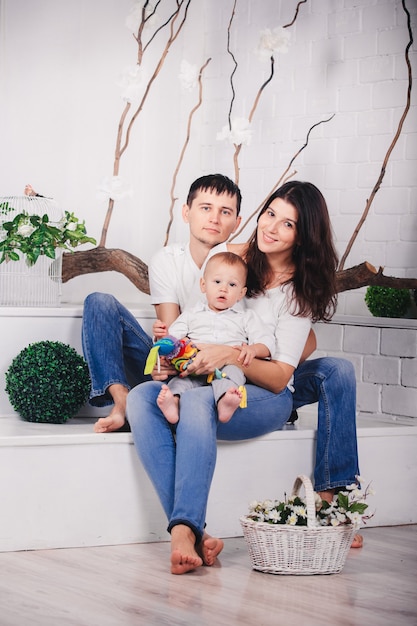 Familia agradable en el fondo del estudio en un interior moderno y luminoso en el interior. Sonriente joven madre y padre con hijo hijo posando juntos y sentados en el sofá.