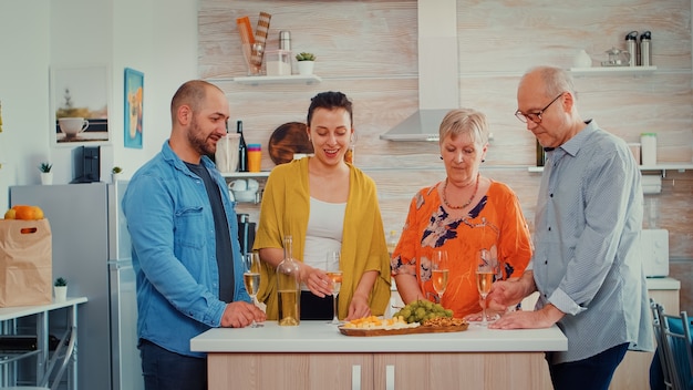 Família alargada e feliz a tilintar e a estarem felizes por se verem. pessoas de duas gerações conversando, sentadas ao redor da mesa, brindando e celebrando um evento bebendo uma taça de vinho branco.