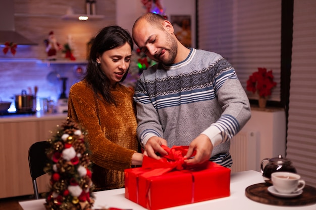 Familia alegre abriendo regalo decorado de Navidad con cinta durante las vacaciones de Navidad