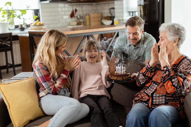 Foto família alegre comemora aniversário de avó com bolo em sala de estar aconchegante