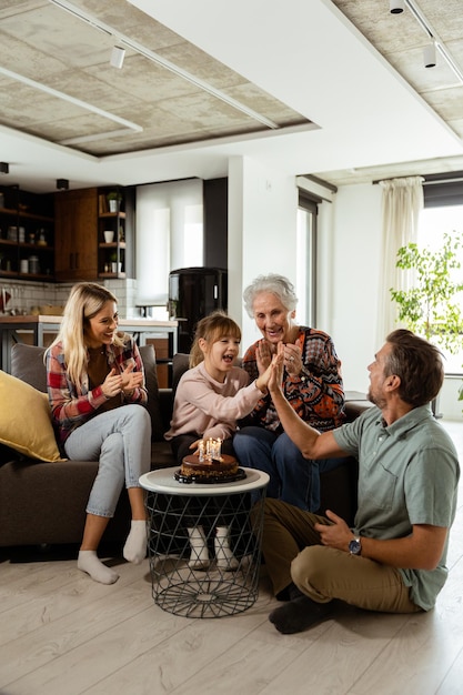 Foto família alegre comemora aniversário de avó com bolo em sala de estar aconchegante