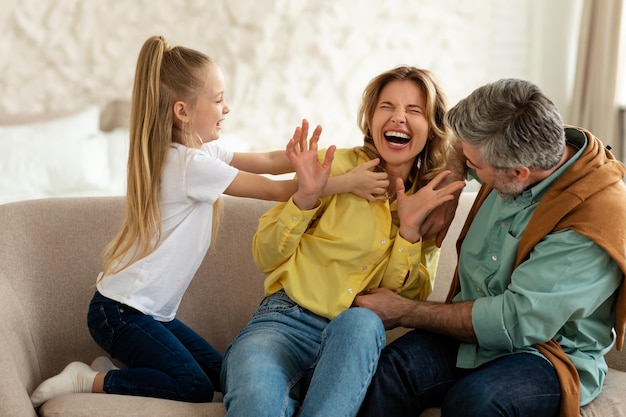 Família alegre de três se divertindo fazendo cócegas no interior