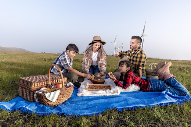 Familia alegre descansando en un picnic en la naturaleza en el parque eólico