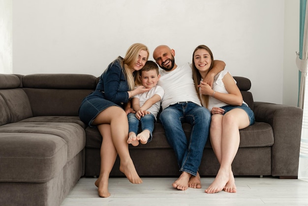 Familia alegre está sentada en el sofá en casa padre calvo con barba abraza a su esposa con niños concepto familiar pasatiempo familiar