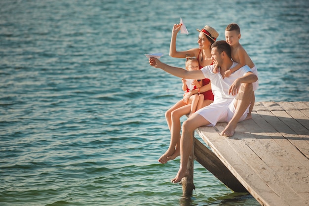 Familia alegre feliz en el muelle cerca del agua divirtiéndose. Adorables niños jugando con sus padres.