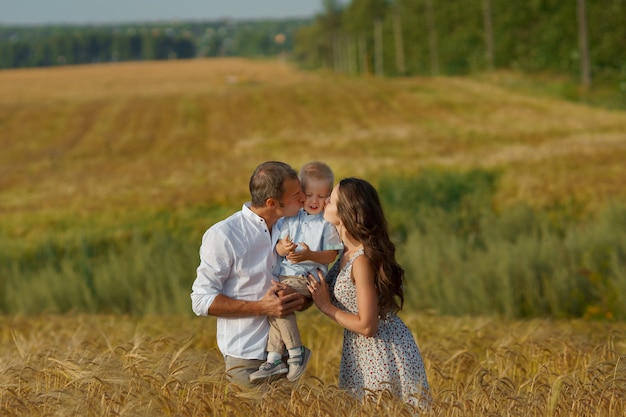 Familia alegre joven caminando por un campo de trigo. Madre, padre y niño pequeños ocios juntos al aire libre. Los padres y el niño en la pradera de verano.