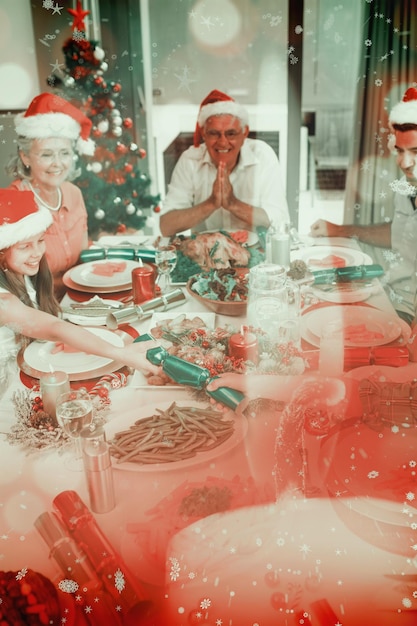 Familia alegre en la mesa de comedor para la cena de navidad contra la quema de velas contra el fondo festivo