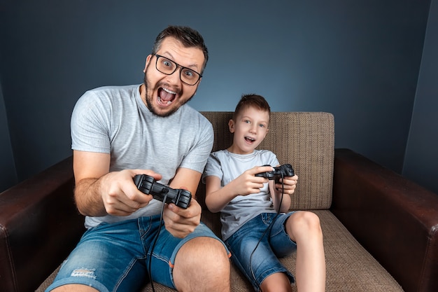 Una familia alegre, padre, madre e hijo juegan en la consola, los videojuegos, reaccionan emocionalmente sentados en el sofá. Día libre, entretenimiento, ocio, pasar tiempo juntos.