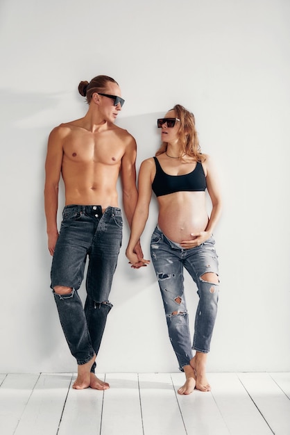 Família alegre retrato de pessoas recém-casadas e isoladas grávidas esperando bebê vestindo jeans e óculos de sol sobre fundo branco