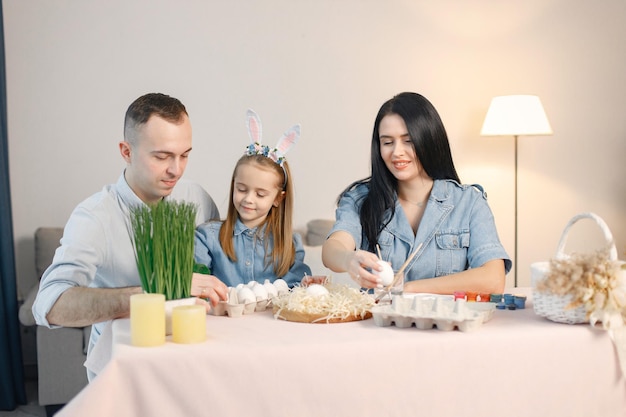 Família alegre reunindo-se à mesa na cozinha leve moderna e pintando ovos de páscoa juntos