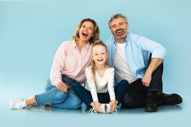 Familia alegre riendo juntos sentados sobre fondo azul de estudio