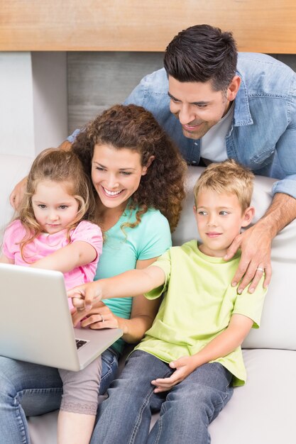 Família alegre sentada no sofá olhando laptop