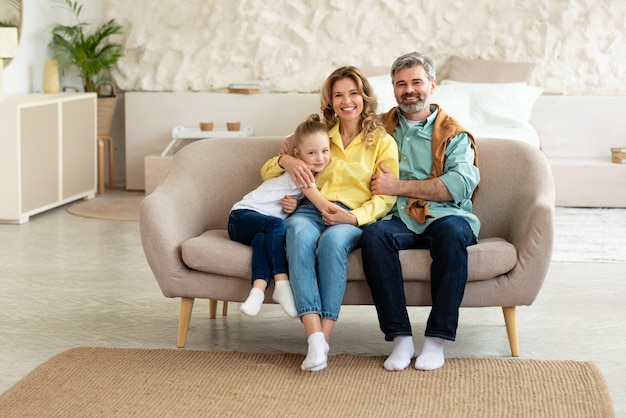 Familia alegre sentada en el sofá en la moderna sala de estar interior