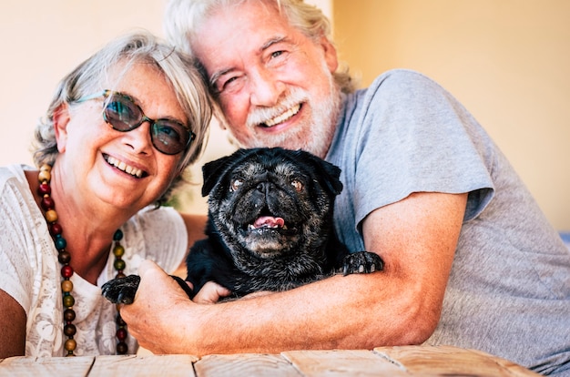 Familia alternativa alegre con ancianos pareja senior y divertido perro pug negro abrazan juntos en actividad de amor