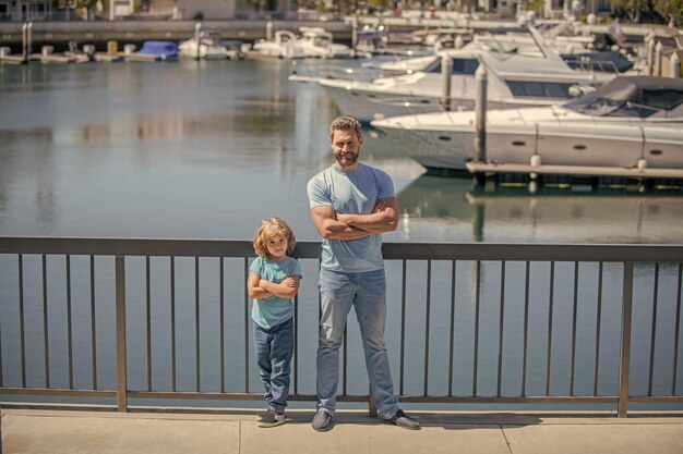 Família amigável de pai e filho relaxa olhando iates no porto de verão