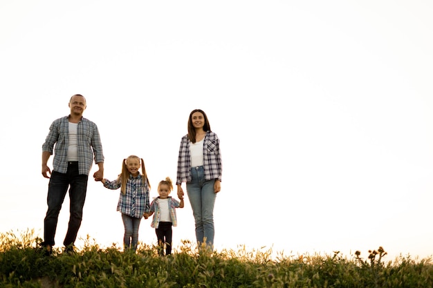 Família amigável feliz com crianças caminha ao pôr do sol no campo contra o céu Pais e filhos andam de mãos dadas Duas irmãs e um jovem pai e mãe Conceito de família feliz juntos