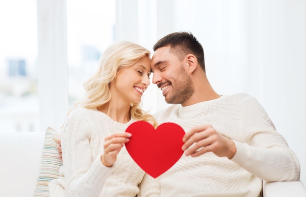 família, amor, dia dos namorados e conceito de pessoas - casal feliz com coração vermelho abraçando no sofá em casa