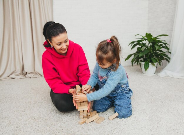 Familia amorosa feliz jugando con bloques de madera y divirtiéndose. Madre y su hija jugando juntas.