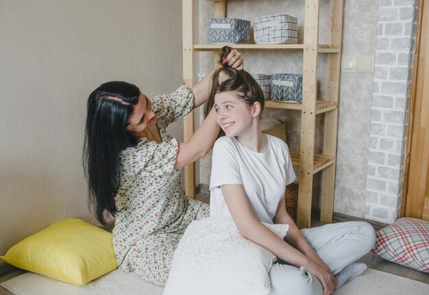 Familia amorosa feliz Una madre peina el cabello de su hija mientras está sentada en el suelo de una habitación