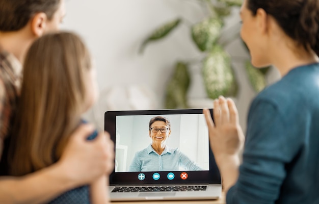 Familia amorosa feliz. Padre, madre e hija usando una computadora portátil para una conversación remota con la abuela. Mamá divertida, papá y un niño encantador se divierten quedándose en casa.