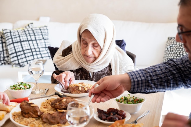 Família árabe a jantar juntos numa mesa de madeira com o pai, a mãe, o avô, a avó e o filho.