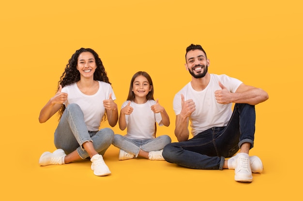 Família árabe alegre gesticulando polegares para cima aprovando algo fundo amarelo