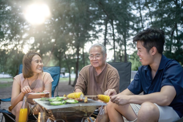 Familia asiática con ancianos bebiendo y haciendo barbacoa juntos. Cocinar barbacoa a la parrilla para la cena durante el campamento en verano.