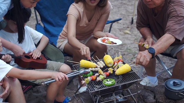 Família asiática com sênior bebendo e fazendo churrasco juntos. Cozinhar churrasco grelhado para jantar durante o acampamento no verão doliday.