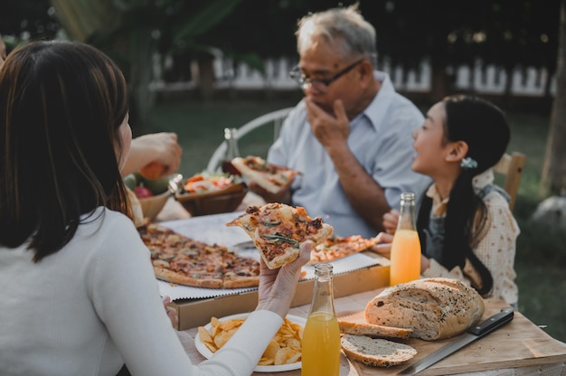 Família asiática comendo pizza no jardim em casa. Pai com filho e avô estilo de vida no quintal.