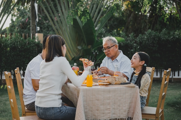 Familia asiática comiendo pizza en el jardín en casa. Padre con estilo de vida de niño y abuelo en el patio trasero.